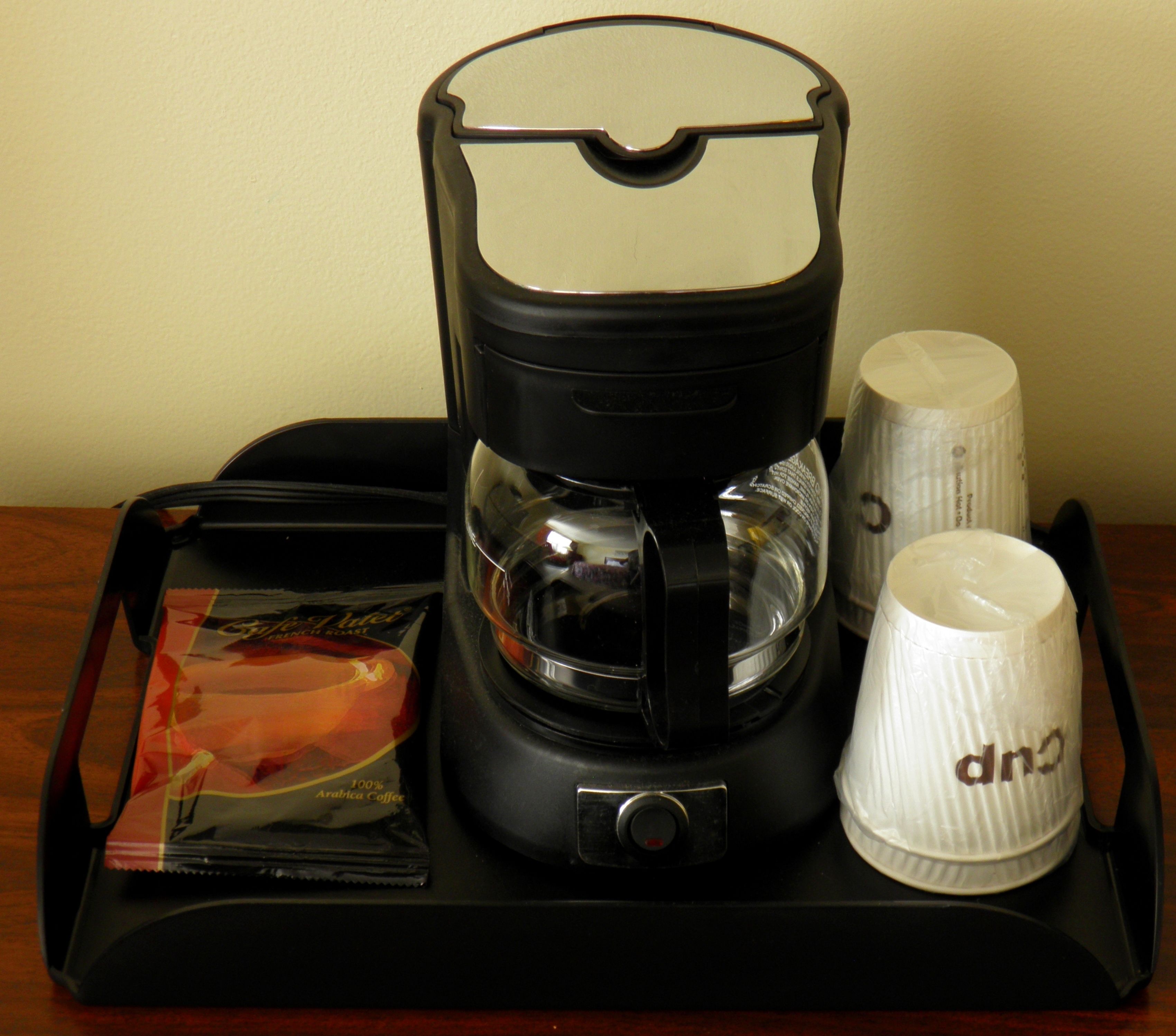 A coffee maker with a coffee pod, a white mug, and a glass carafe on a tray.
