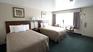 A hotel room with two beds, a desk, a chair, and a window with curtains. - Travelers Inn (Brunswick)