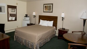A hotel room with a large bed, bedside tables, a desk, a chair, and a dining table.