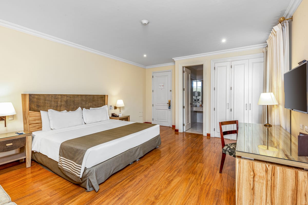 Une chambre d’hôtel avec un grand lit, des tables de chevet, une télévision et une table en verre.