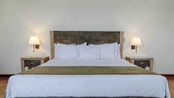 A neatly made bed with white linens and a green throw blanket, flanked by two bedside tables with lamps.