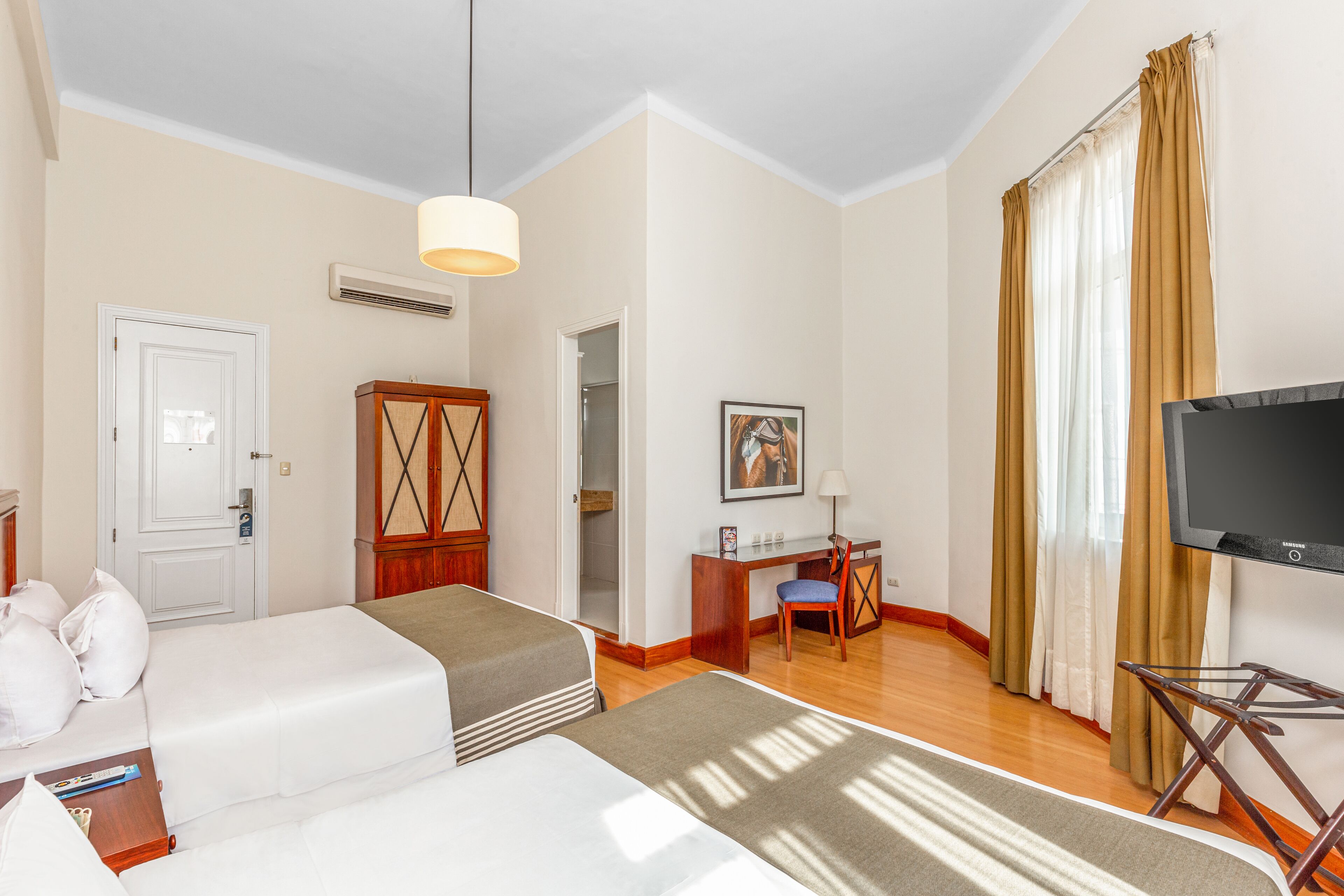 A hotel room with two beds, a desk, a chair, a television, and a wardrobe.