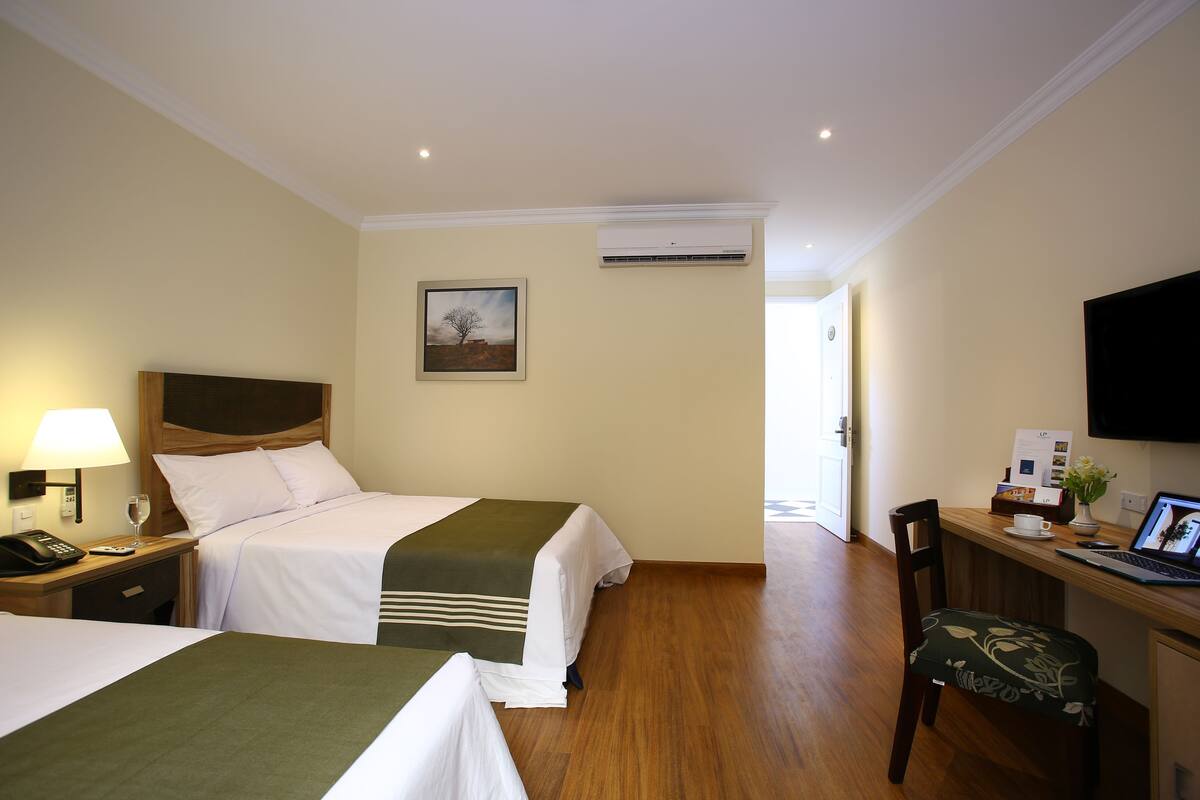 Une chambre d’hôtel avec deux lits, un bureau avec un ordinateur portable, une chaise, un téléphone, une lampe et un appareil de climatisation.