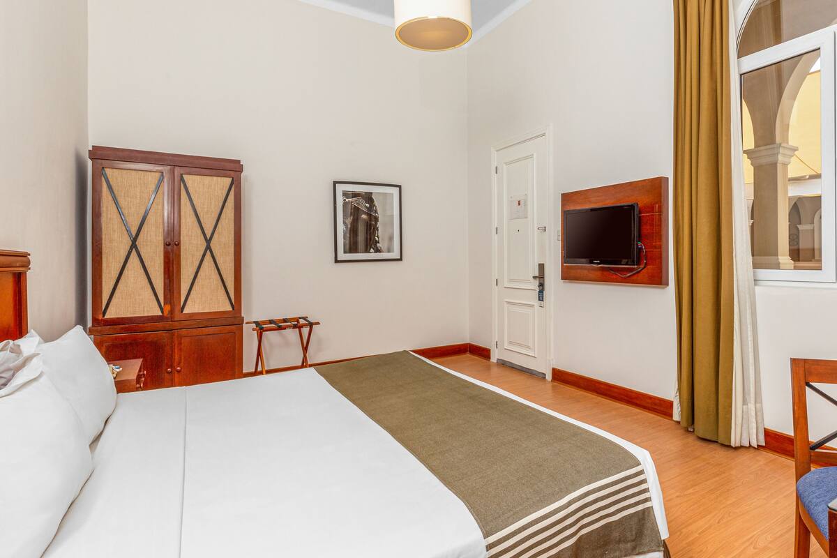 Une chambre d’hôtel avec un lit, une armoire, une télévision et une fenêtre avec des rideaux.