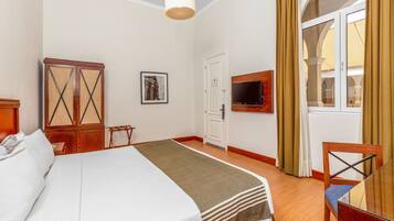 Una habitación de hotel con cama, armario, televisión y ventana con cortinas.