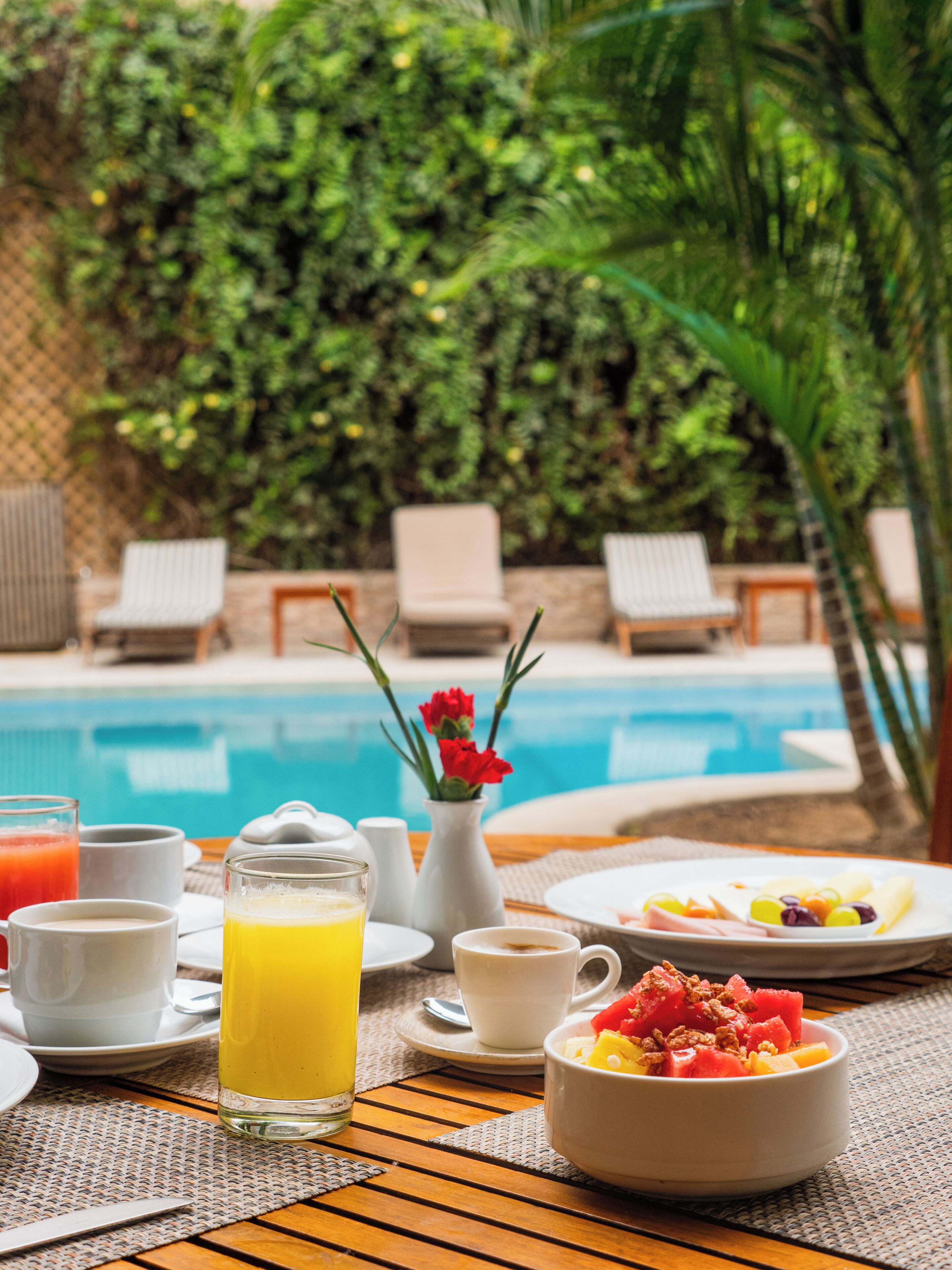 Mesa de café da manhã com piscina e vegetação ao fundo.