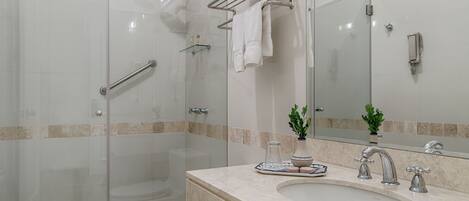 Un baño moderno con ducha de vidrio, inodoro blanco, lavabo con encimera de mármol y espejo con toallero encima.