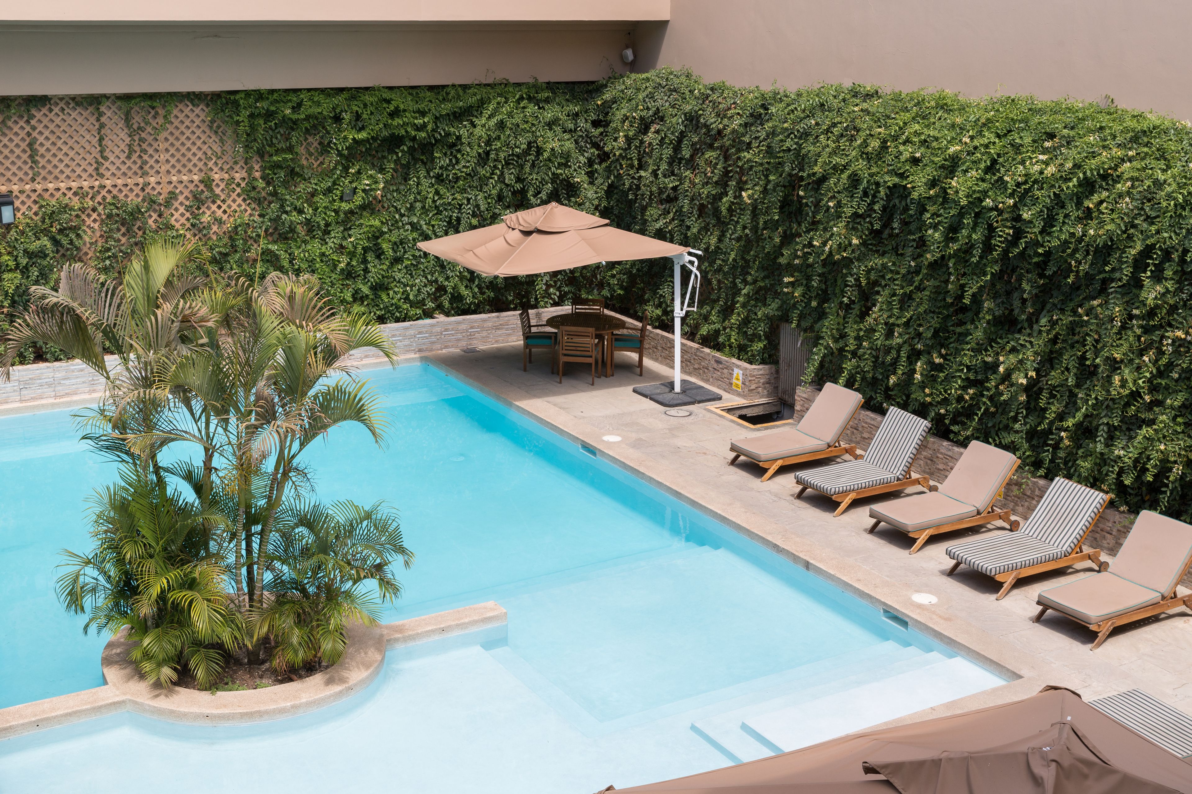 Ein Pool mit Liegestühlen und einem Tisch, umgeben von viel Grün.