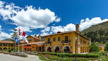 A yellow building with arched windows and a red roof, surrounded by a landscaped garden with flowers and a flagpole.