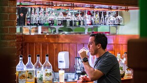 Un hombre sentado en un bar con un letrero de neón que dice "Corona".