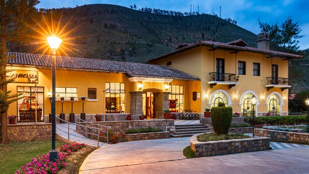 Un hotel con fachada amarilla, varios balcones y un acceso ajardinado con escalones y macetas.