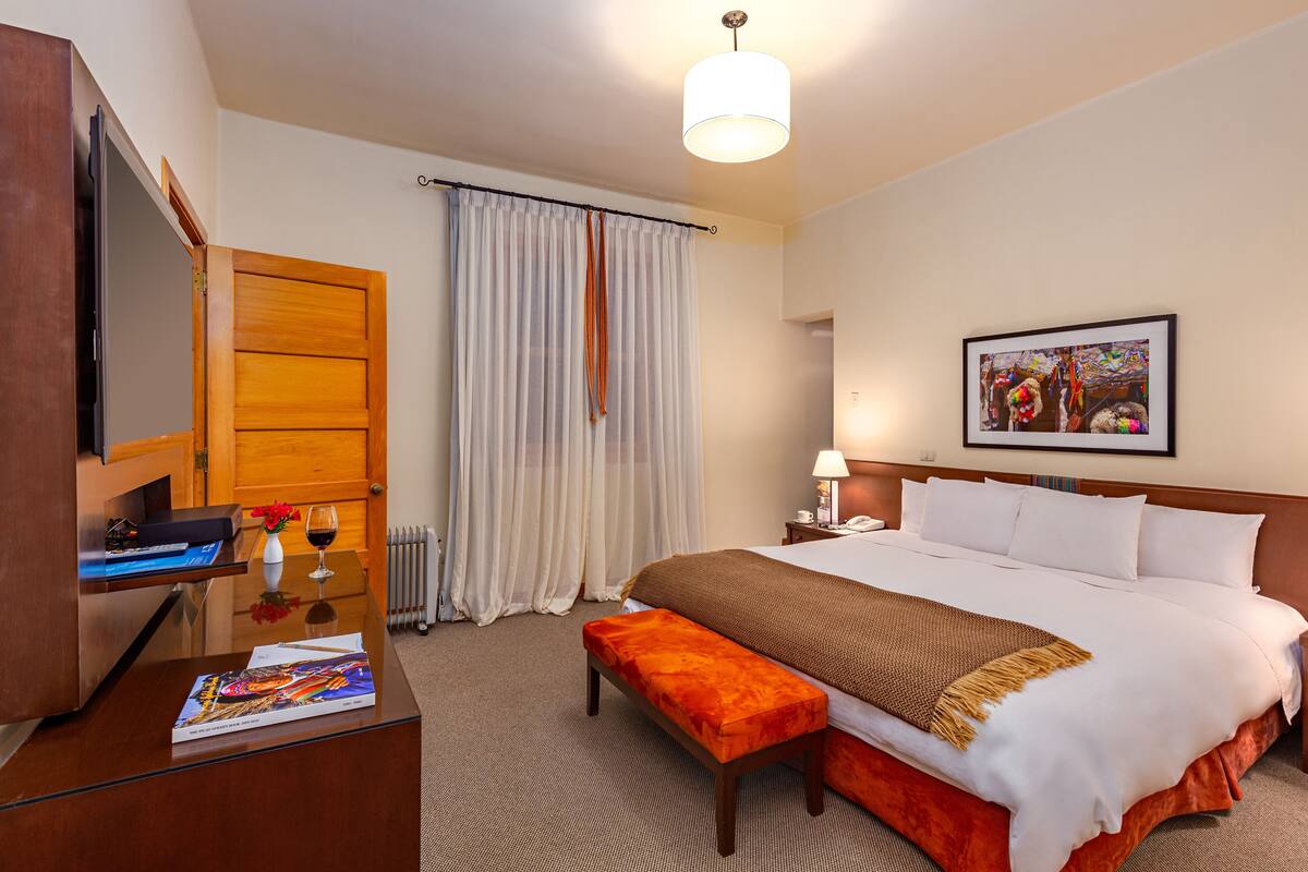 A hotel room with a bed, a desk with a computer, a lamp, and a painting on the wall.