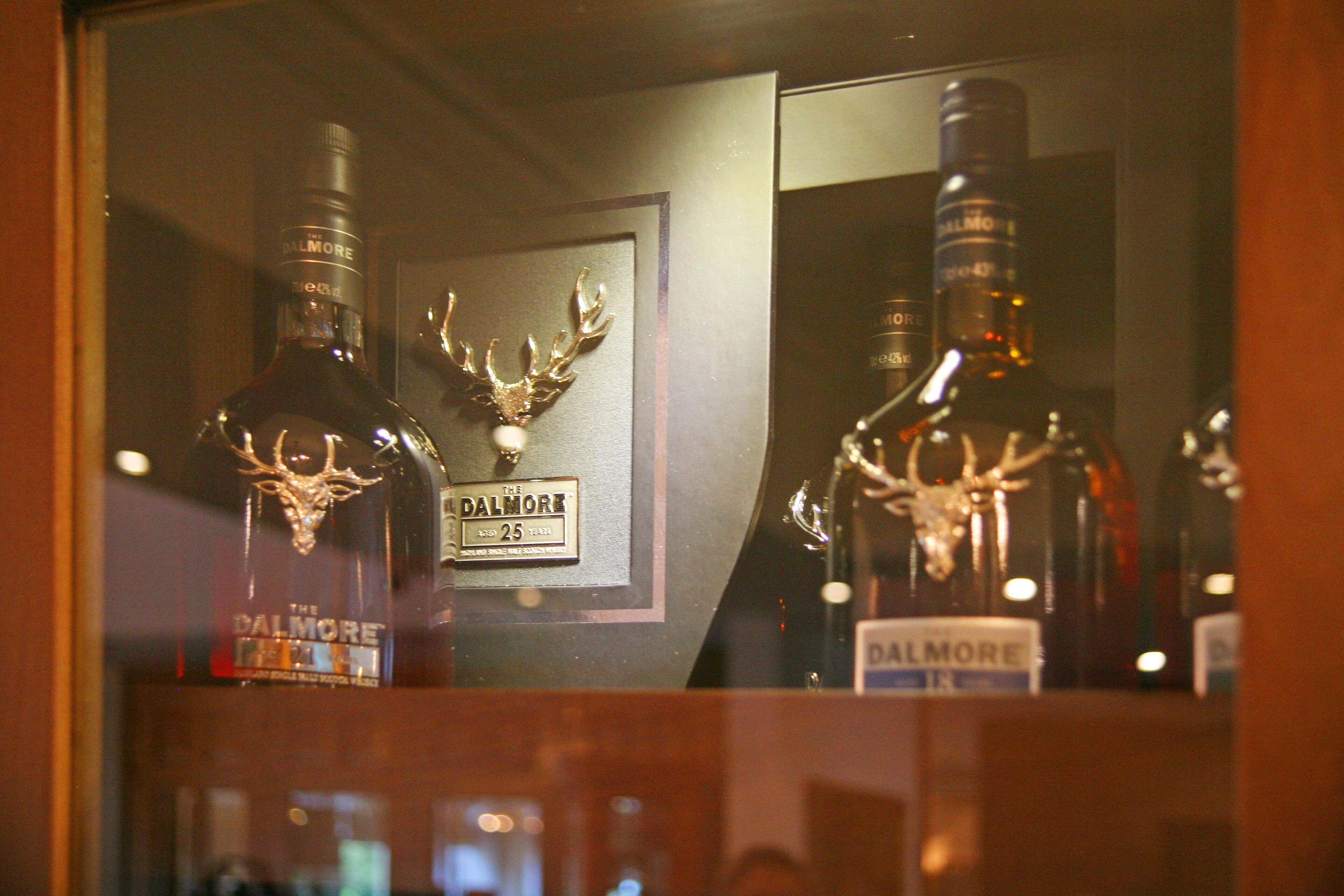 A display of liquor bottles with a deer antler decoration and a framed sign.