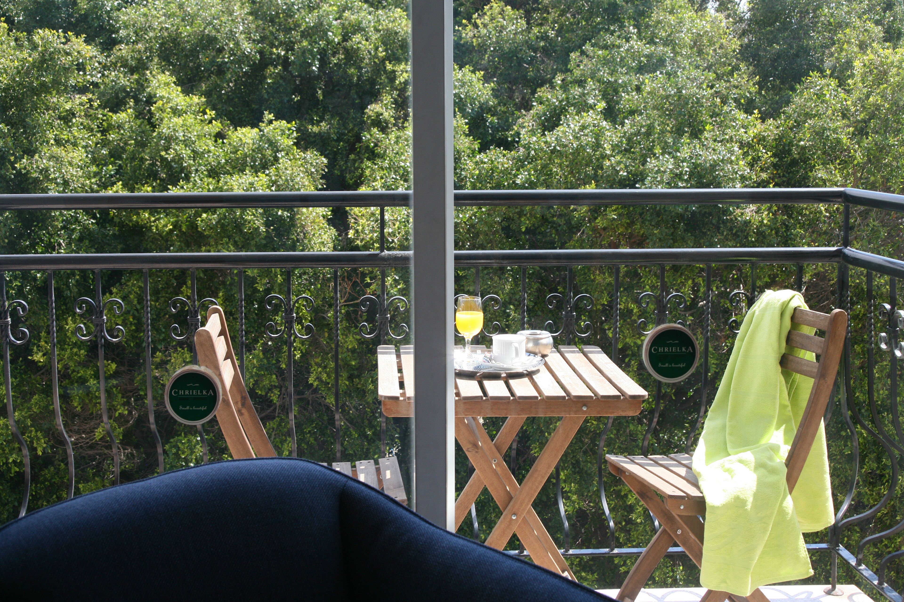 A balcony with a wooden table and chairs, a towel hanging on a chair, and a sign with the name 'CHREI' visible.