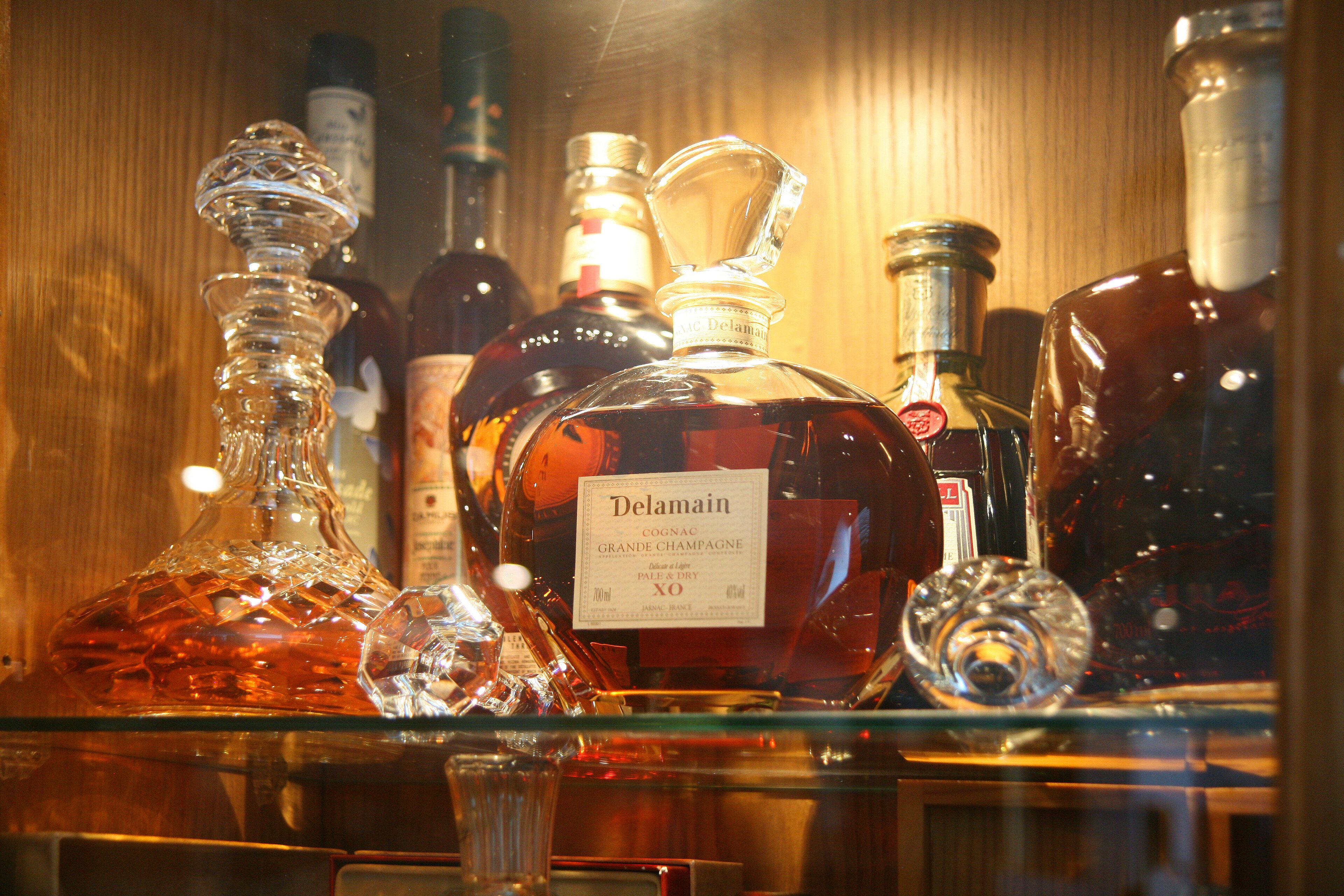 A variety of bottles, including a prominent Delamain cognac bottle, displayed on a shelf.