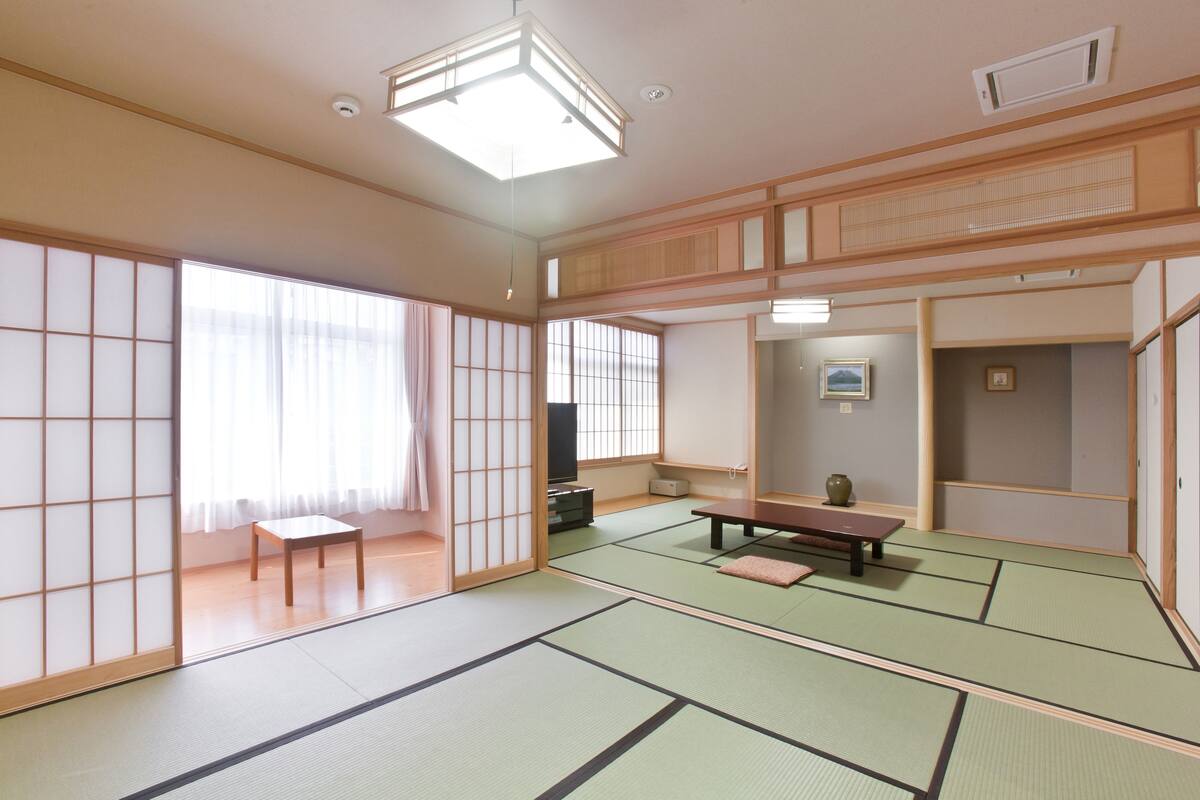 Ein traditioneller japanischer Raum mit Tatami-Boden, einem niedrigen Tisch, einer Bank, Schiebetüren und einem Fernseher.