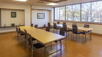 Una sala de conferències amb una taula llarga i cadires, grans finestres que donen a vistes d'arbres, i dos quadres a les parets.