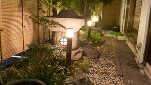 Un chemin de jardin bien entretenu, bordé de pierres, entouré d’une végétation luxuriante et agrémenté d’une lanterne en pierre.