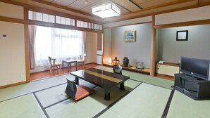 Une pièce de style japonais traditionnel, avec un sol recouvert de tatamis, une table basse, des chaises, un téléviseur et une porte coulissante donnant sur une autre pièce.