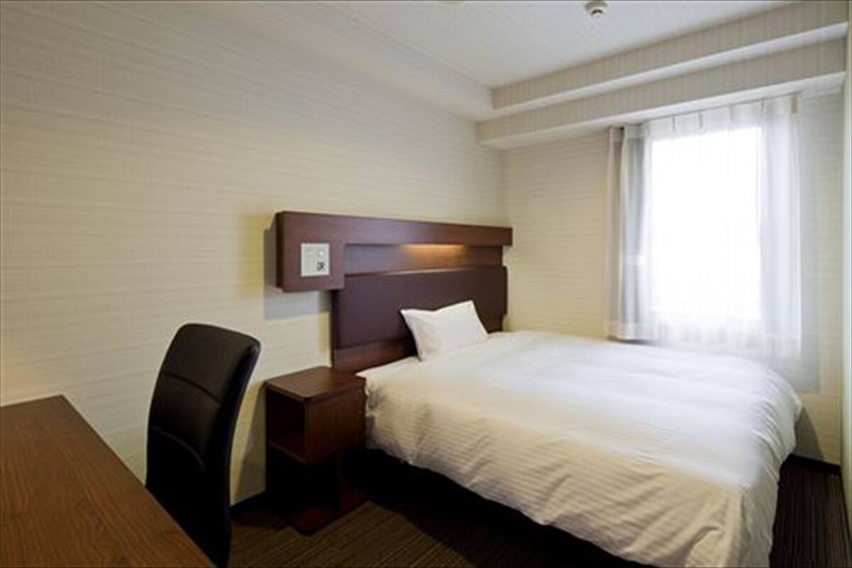 A hotel room with a bed, a desk, and a chair.