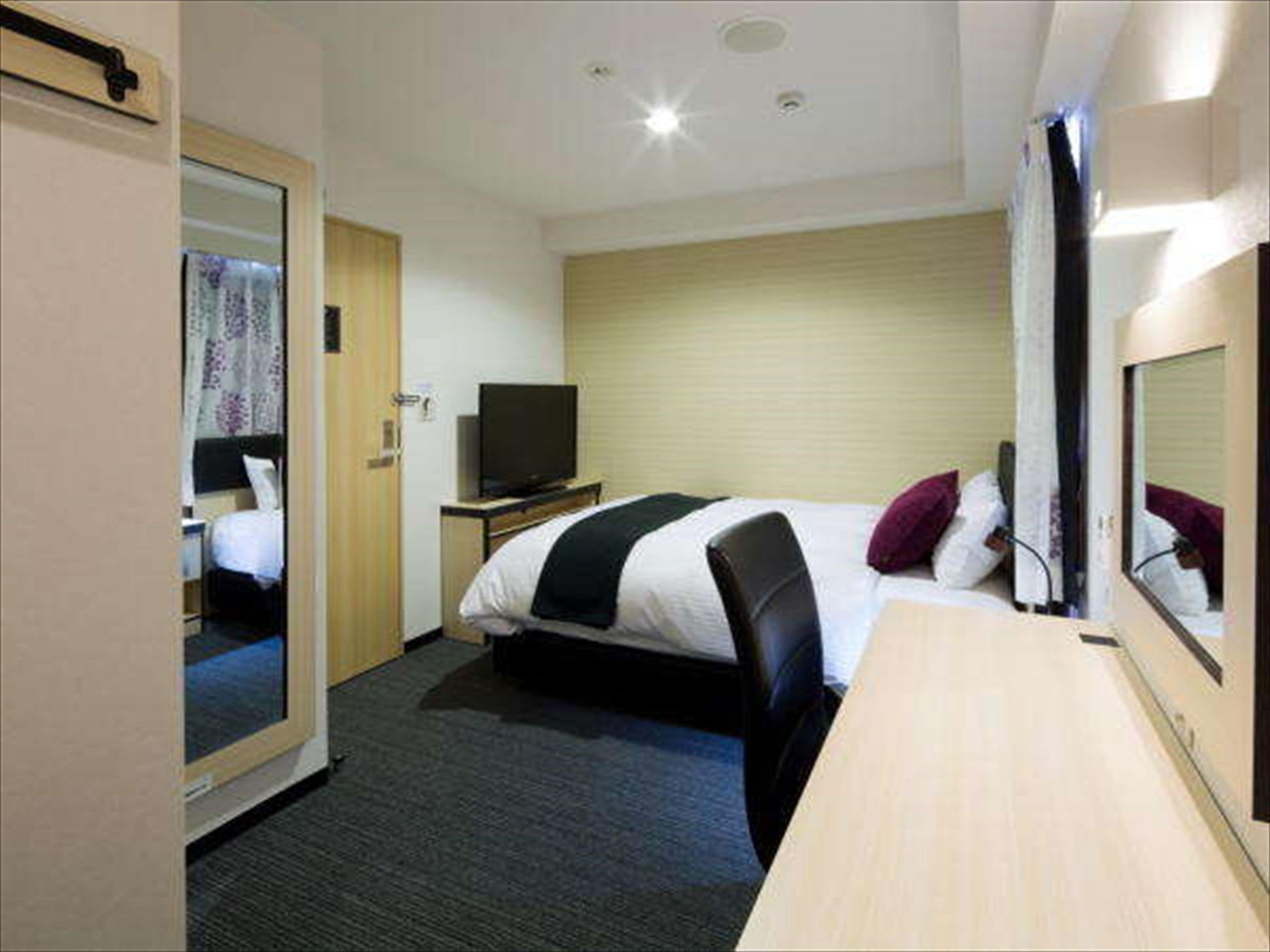 A hotel room with a bed, a television on a stand, a desk, and a mirror.