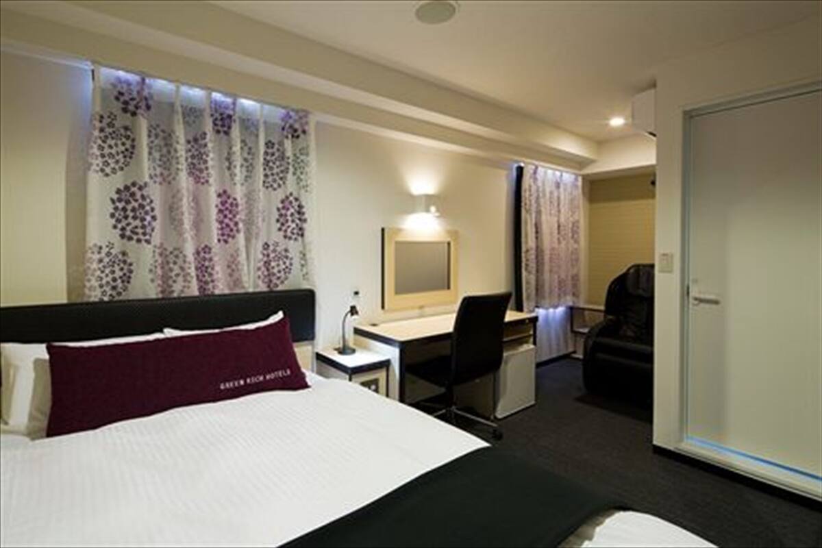 A hotel room with a bed, a desk, a chair, a mirror, and a wardrobe.