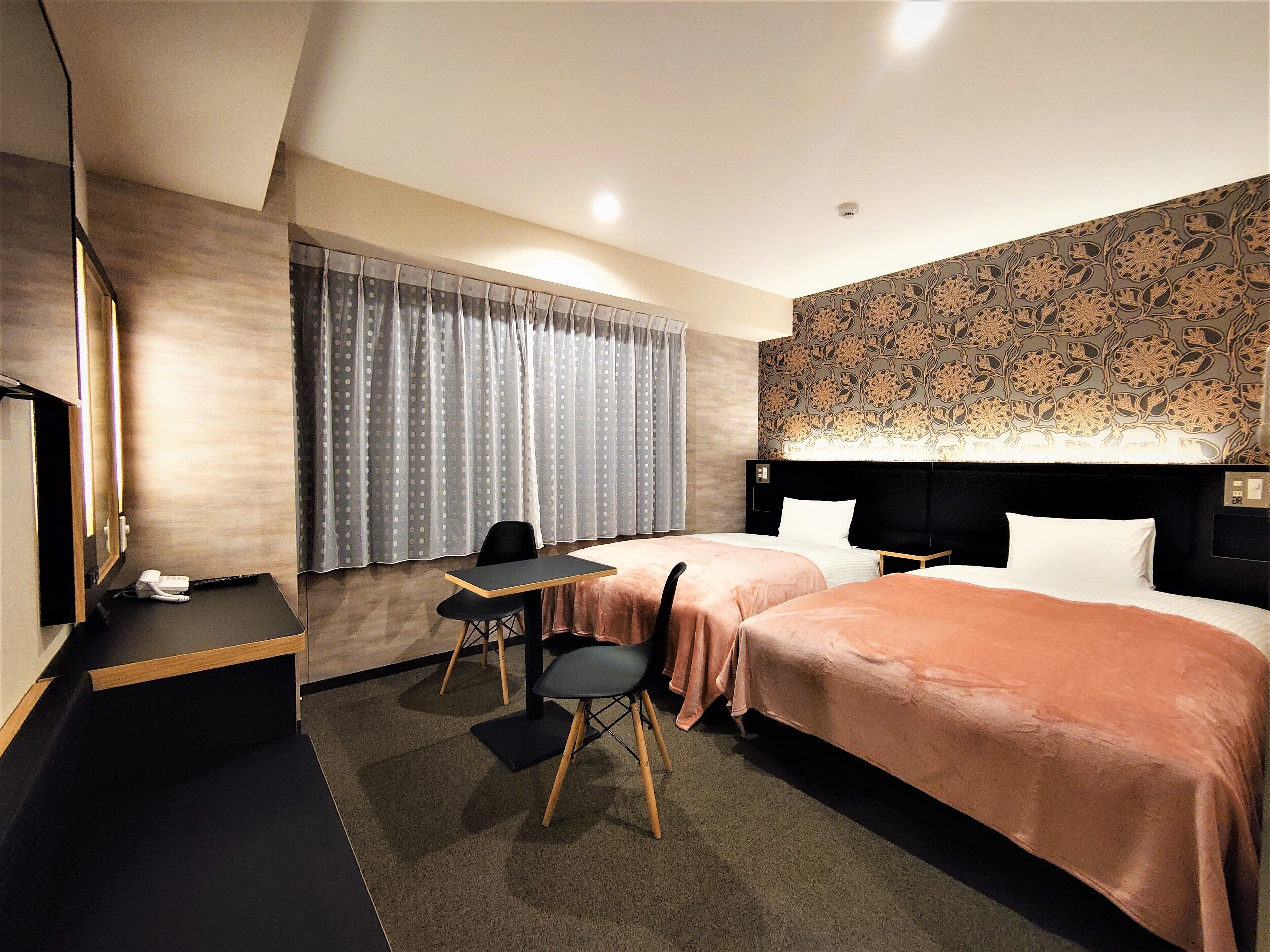 A hotel room with two beds, a desk, a chair, and a telephone.