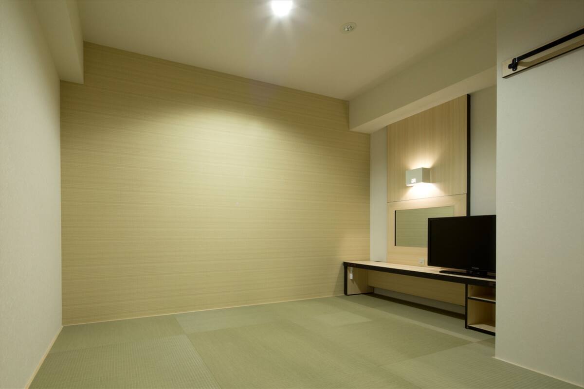 A modern hotel room with a large mirror, a flat-screen TV, and a small seating area.