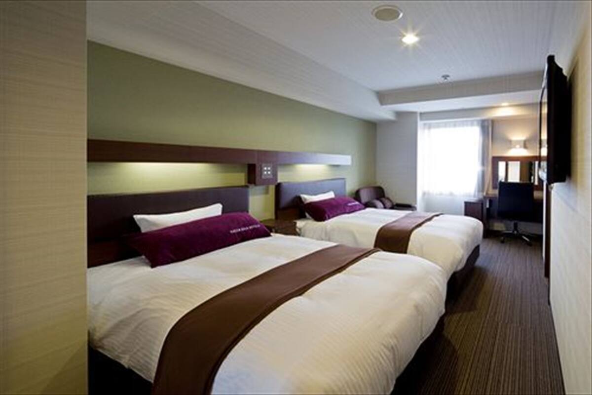 A hotel room with two beds, a desk, and a television.