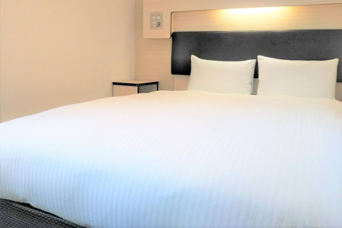 A neatly made bed with white linens, a black headboard, and a small bedside table.