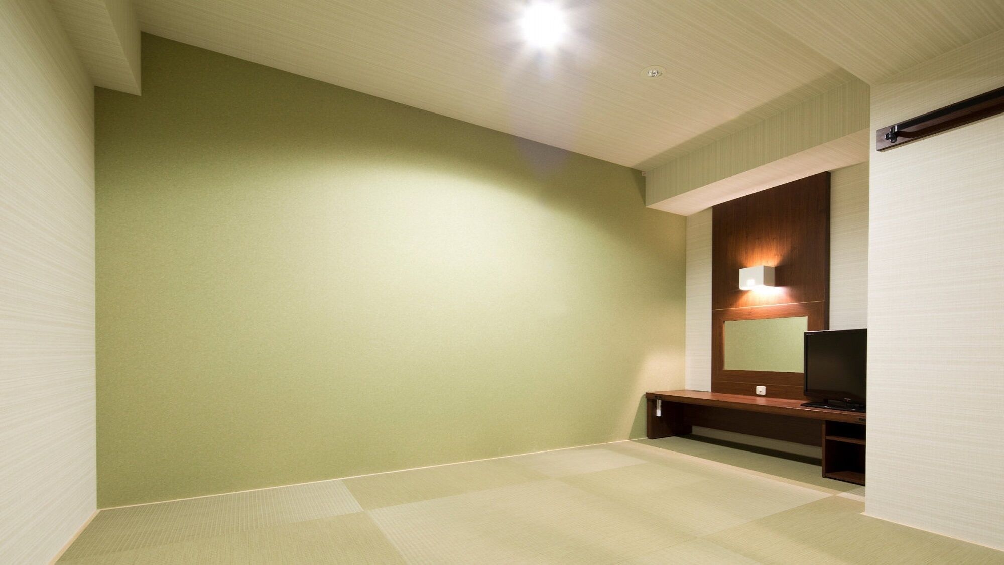 A room with a green wall, a wooden bench, a flat-screen TV, and a ceiling light.