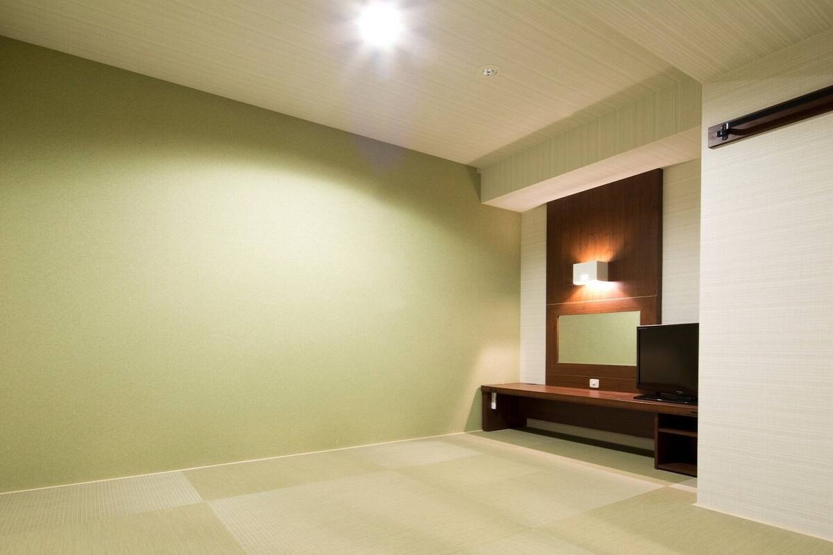 A room with a green wall, a wooden bench, a flat-screen TV, and a ceiling light.