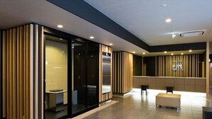 A modern hotel lobby with a reception desk, seating area, and a glass elevator.