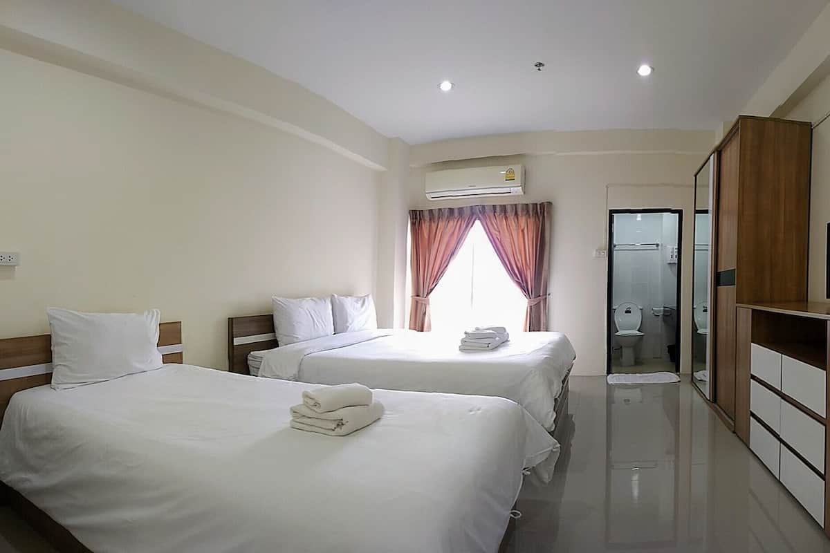 A hotel room with two beds, a TV, a wardrobe, and a bathroom visible through a glass door.