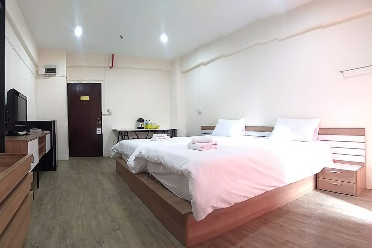 A hotel room with a bed, bedside tables, a desk with a chair, a TV, and a door.
