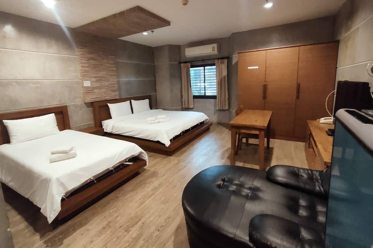 A hotel room with two beds, a wooden desk, a leather chair, and a wardrobe.