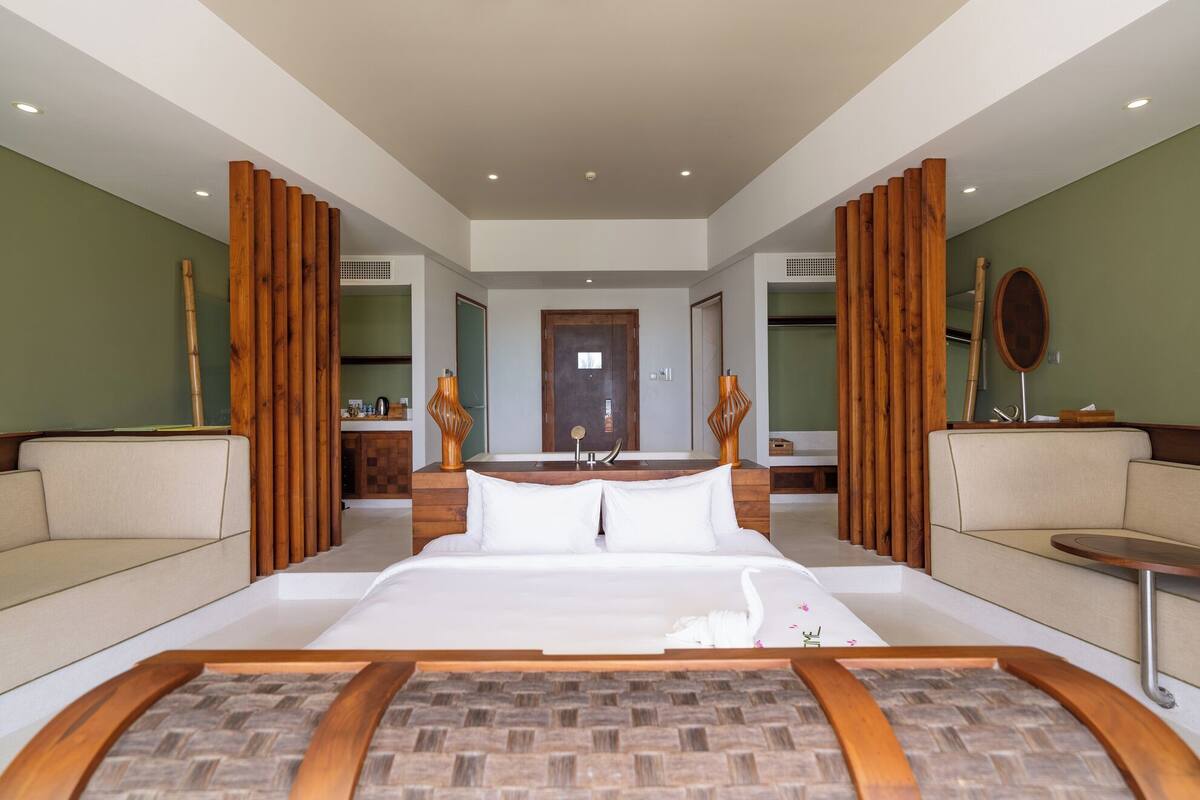 A spacious hotel room with a large bed, two sofas, a small table, and wooden decor elements.