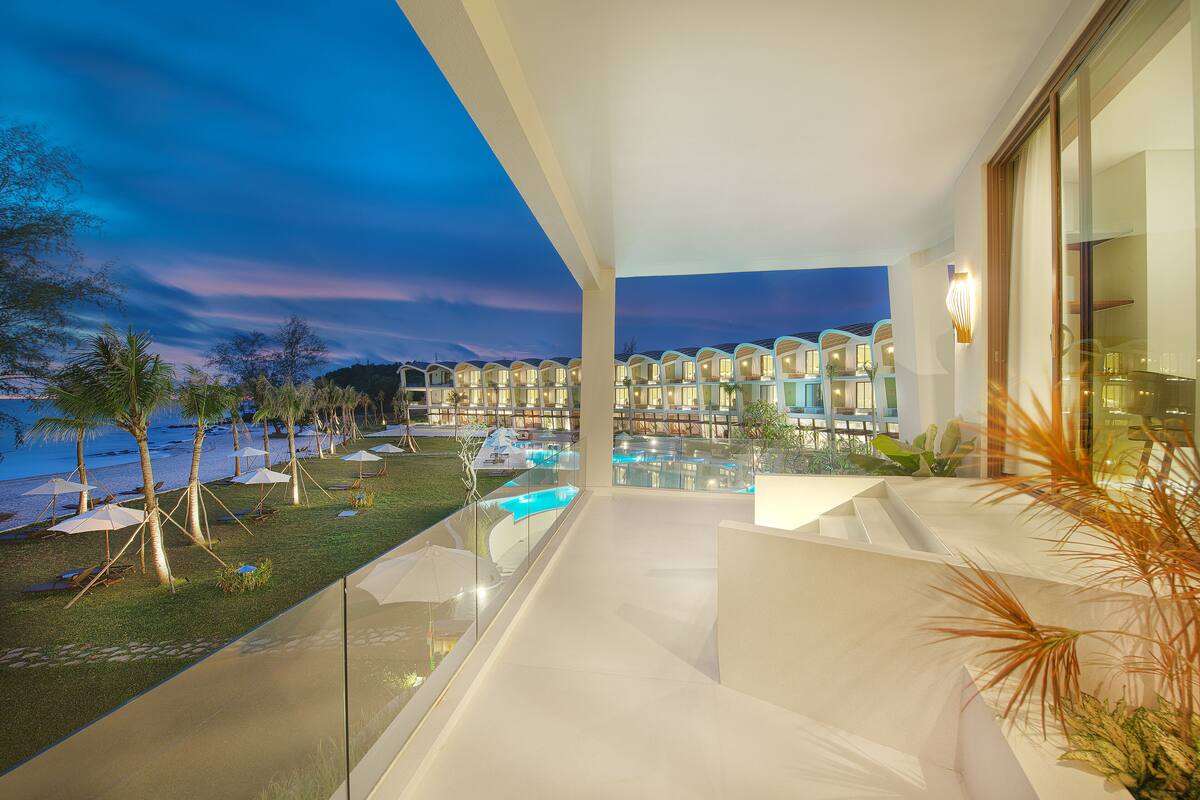 A modern hotel with a pool area, outdoor seating, and a view of the beach at dusk.