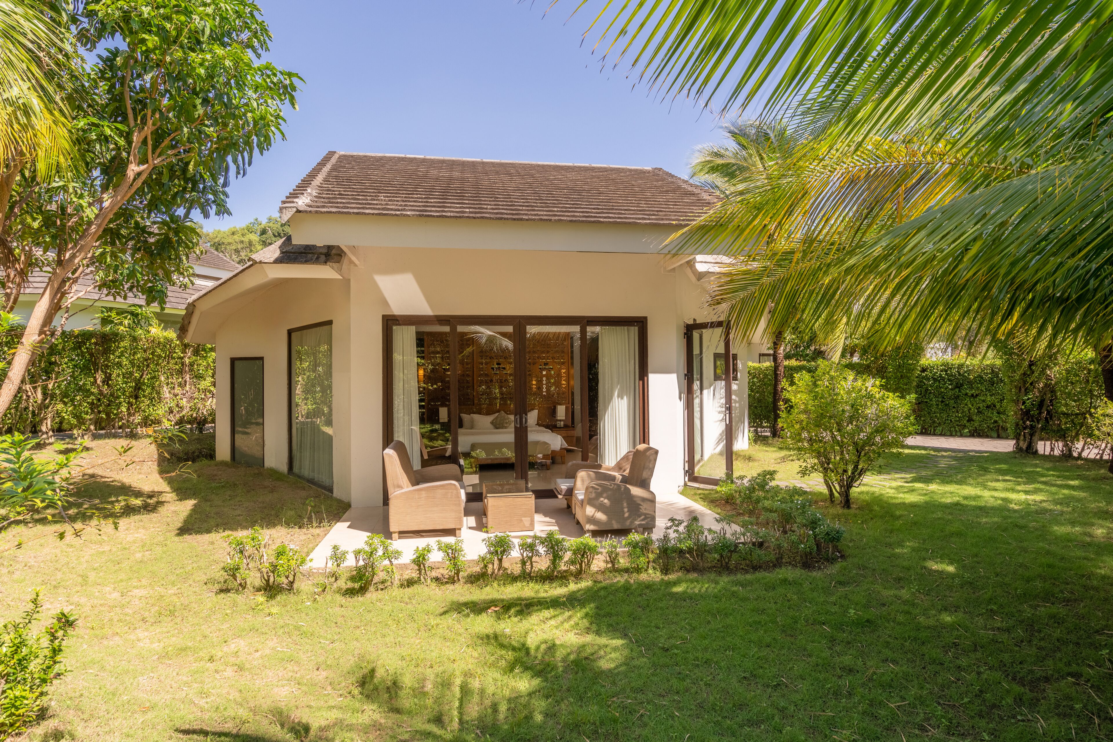 A modern house with a patio area featuring outdoor furniture and a glass door leading to a room with a bed and seating area.