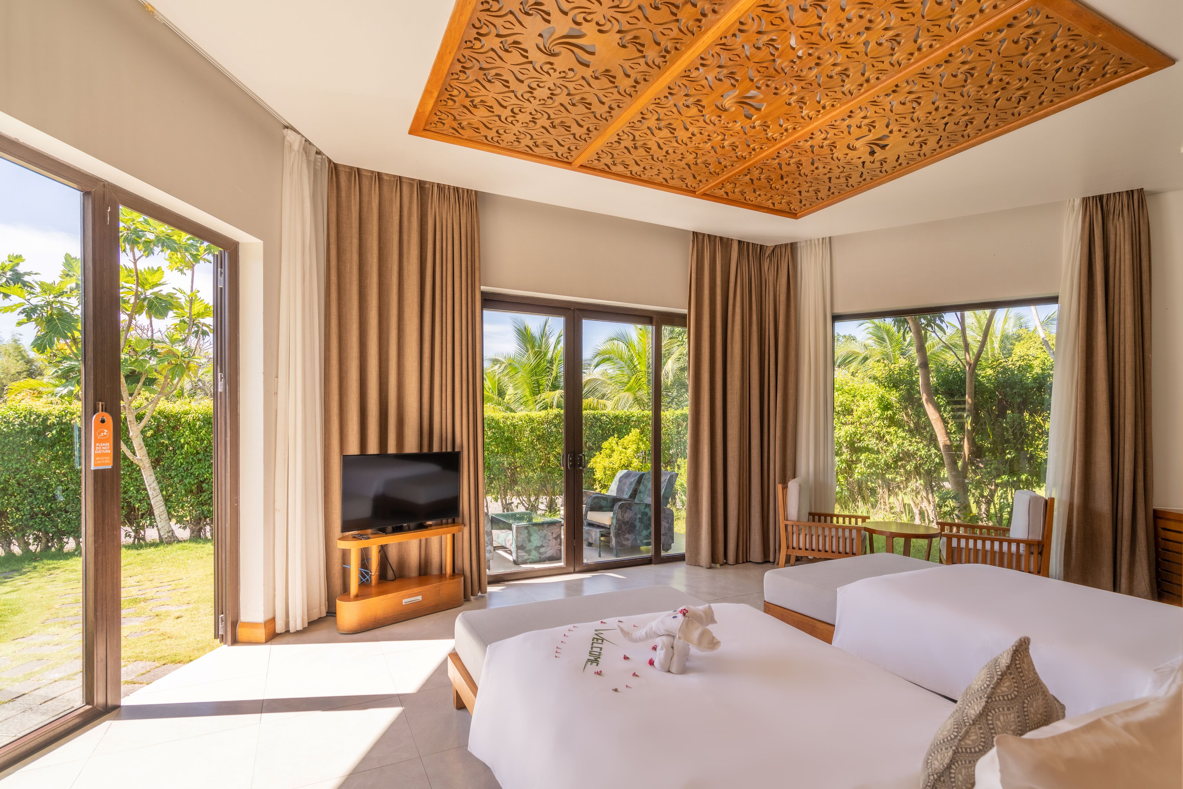 A modern hotel room with a large bed, a TV, and a balcony with a view of palm trees.