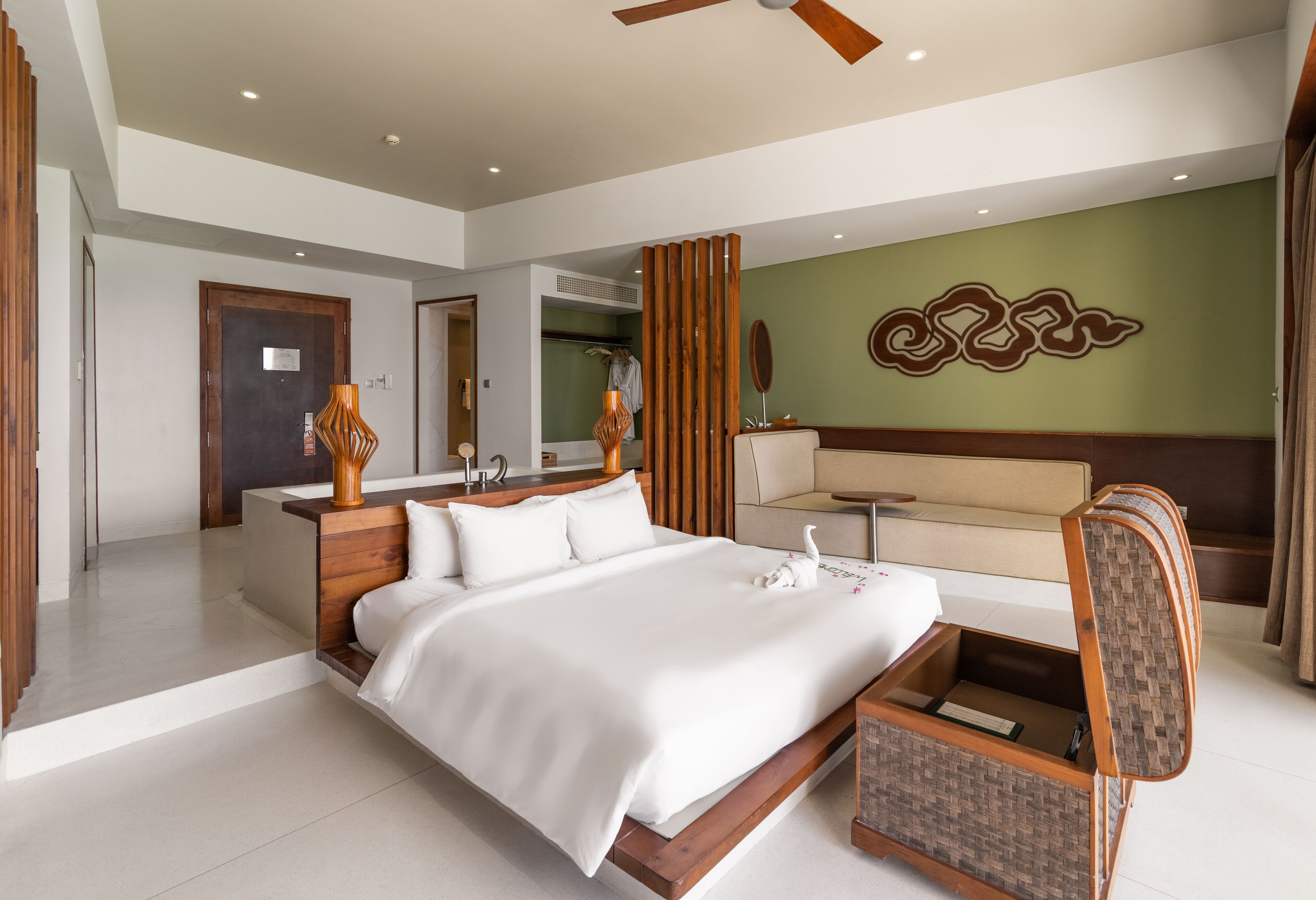 Una habitación de hotel moderna con una cama grande, un cabecero de madera, una mesita pequeña y un sofá.