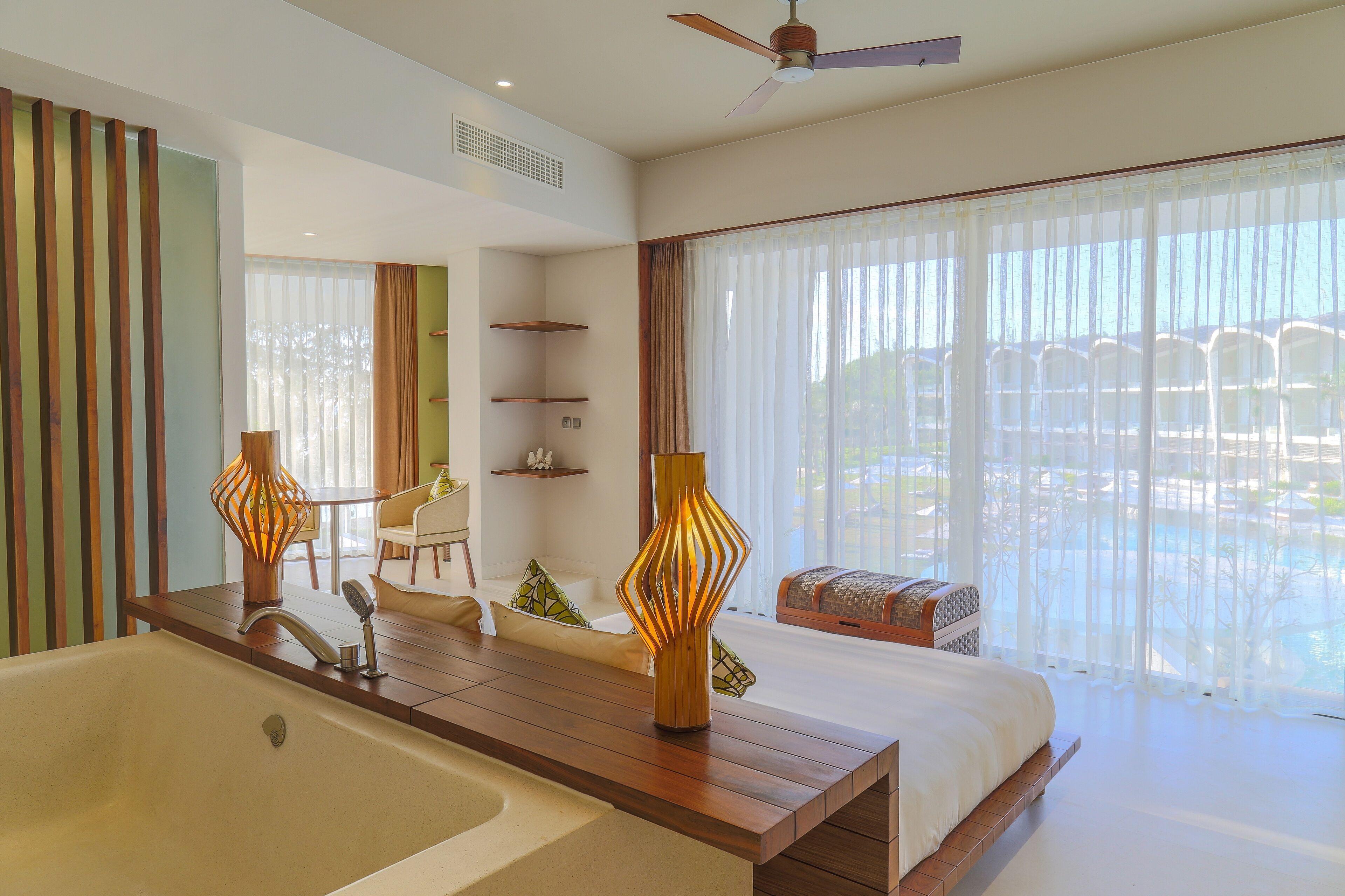 A modern hotel room with a large bed, a wooden desk, a view of a pool, and a ceiling fan.