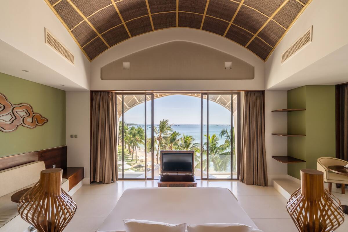 A hotel room with a large bed, a TV, and a view of the ocean.