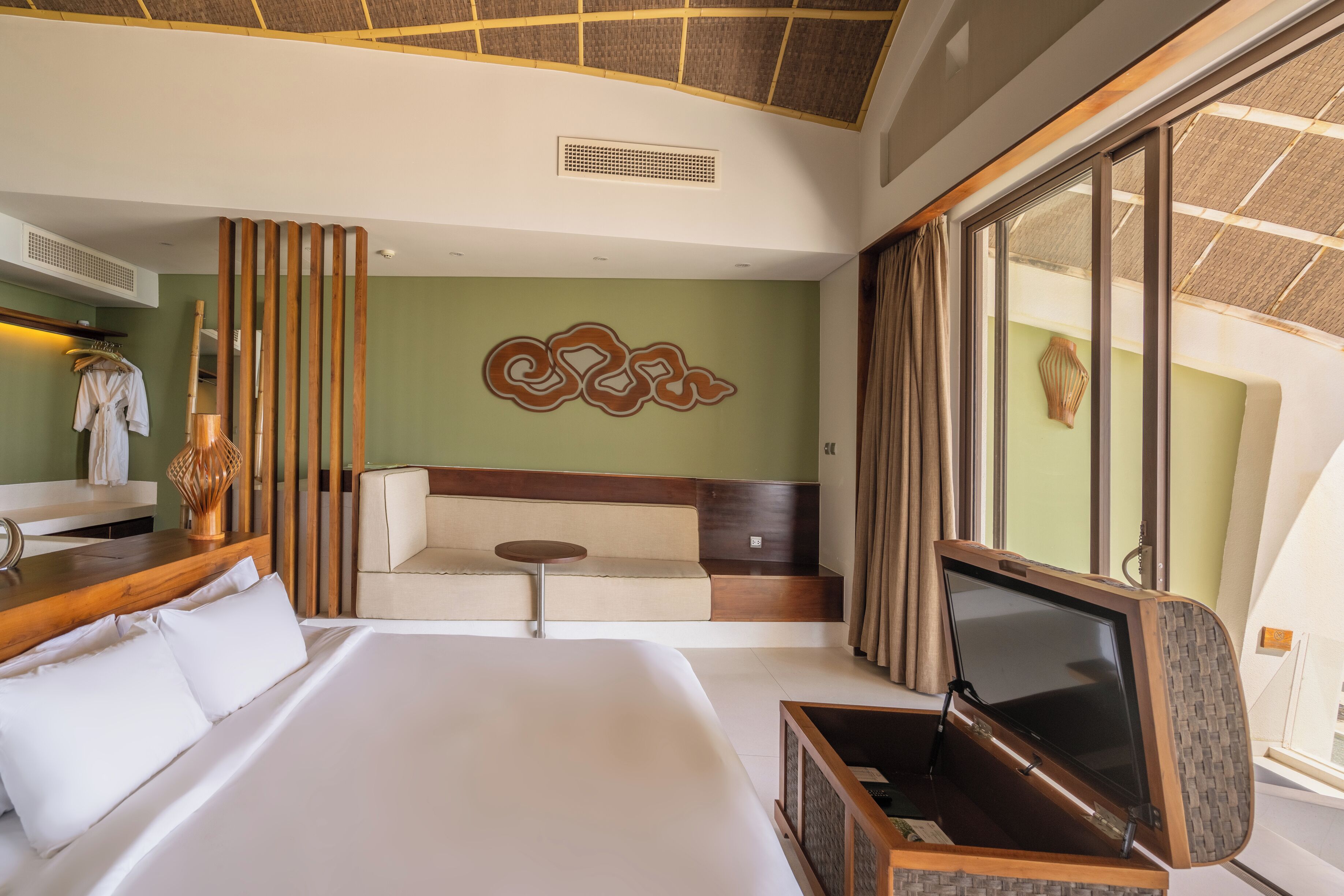 A hotel room with a large bed, a seating area with a sofa and a small table, a TV, and a large window with curtains.