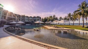 A resort pool area with lounge chairs, umbrellas, and a view of the ocean.