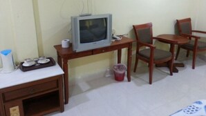 A room with a television on a wooden table, a chair, a small trash bin, and a desk with a telephone. - MNR Motel (Langkawi)