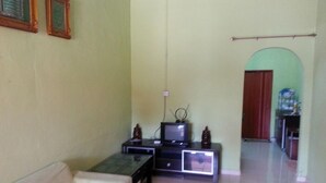 A living room with a sofa, a TV, and a small table. There is a door leading to another room. - MNR Motel (Langkawi)