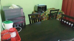 A dining area with a table, chairs, a microwave, a small refrigerator, and a coffee maker. - MNR Motel (Langkawi)