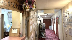 A hallway with a reception desk, a bulletin board with notices, and a floral decoration. - Asakusa Ryokan Toukaisou (Tokyo)