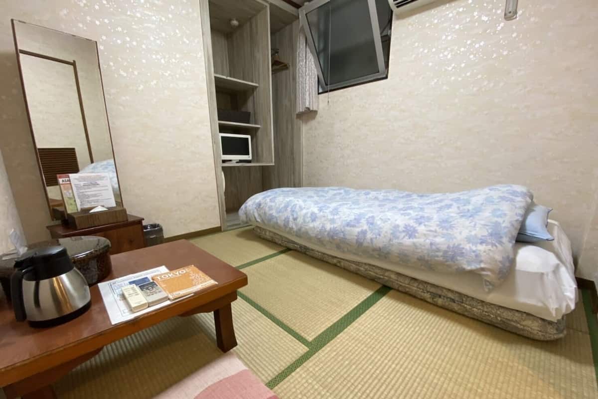Hotelkamer met een bed, een kleine tafel met waterkoker en menukaart, een spiegel en een televisie op een plank.